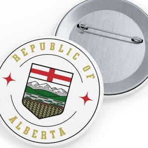 Puede incluir: Dos botones redondos blancos con un alfiler en la parte posterior. Un botón presenta el escudo de armas de Alberta, con el texto "REPUBLIC OF ALBERTA" en dorado. Dos estrellas rojas enmarcan el escudo.