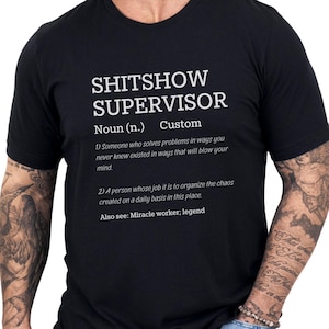 May include: Black crew neck t-shirt with the text "SHITSHOW SUPERVISOR" in white. The text includes a definition of the term. A humorous and unique graphic tee.