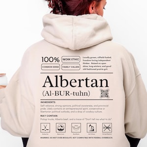 Sand colored (light beige) Alberta hoodie with black ingredient label style back design reading “Albertan (Al-BUR-tuhn)” featuring prairie values icons, independence themed humor, and Alberta pride text