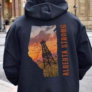 May include: Black hooded sweatshirt with a graphic print of the outline of Alberta, Canada, with a sunset and an oil derrick. The text "Alberta Strong" is printed vertically on the right side of the graphic.