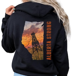 Puede incluir: Sudadera con capucha negra con una impresión naranja del contorno de la provincia de Alberta, una torre de perforación de petróleo y el texto "Alberta Strong".