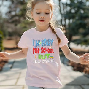 light pink kids crewneck t-shirt that reads “I’m ready for school but is school ready for me?” in colorful letters with fun icons.