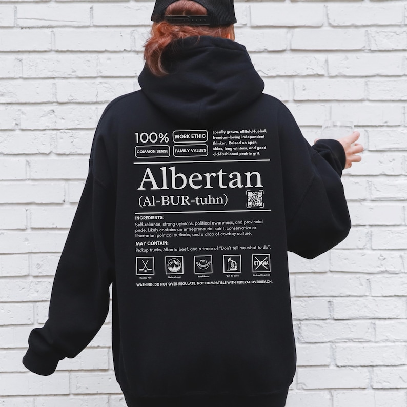 black Alberta hoodie with black ingredient label style back design reading “Albertan (Al-BUR-tuhn)” featuring prairie values icons, independence themed humor, and Alberta pride text
