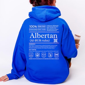 royal blue Alberta hoodie with black ingredient label style back design reading “Albertan (Al-BUR-tuhn)” featuring prairie values icons, independence themed humor, and Alberta pride text