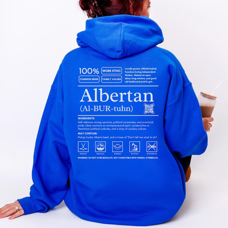 royal blue Alberta hoodie with black ingredient label style back design reading “Albertan (Al-BUR-tuhn)” featuring prairie values icons, independence themed humor, and Alberta pride text