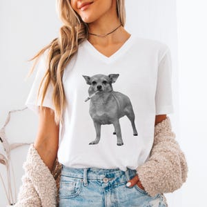 A white unisex vee-neck t-shirt featuring a grayscale image of a Chihuahua standing with a cigarette in its mouth, giving a humorous, meme-style look perfect for dog lovers and fans of funny novelty shirts.