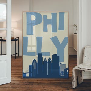 May include: A rectangular wall art print featuring the word PHILLY in large, light blue block letters over a cream background. Below the text is a dark blue silhouette of the Philadelphia skyline, including various skyscrapers and a bridge.