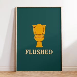 May include: A framed art print featuring a yellow toilet illustration on a teal background. The word "FLUSHED" is printed in a vintage font below the toilet. The artwork is displayed on a wooden floor.