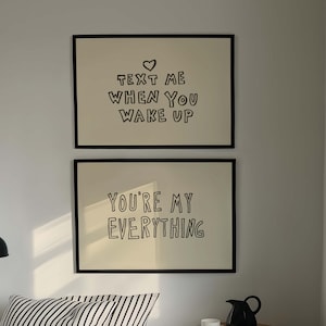 May include: Two rectangular framed wall art prints with black text on a cream background. The top print reads "TEXT ME WHEN YOU WAKE UP" with a heart icon, and the bottom print reads "YOU'RE MY EVERYTHING" in a hand-drawn style font.