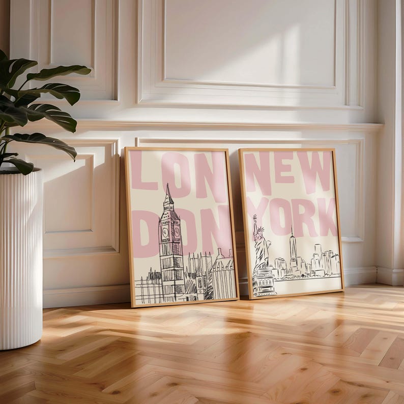 May include: Two framed art prints. One features a sketch of London's Big Ben with the text "LONDON" in pink. The other depicts the New York City skyline with the text "NEW YORK" in pink. Both are in wooden frames.