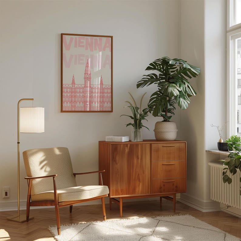 May include: A room interior featuring a framed poster with the word "VIENNA" in pink, a mid-century modern wooden cabinet, a beige armchair, and a floor lamp. A large potted plant and a rug complete the scene.