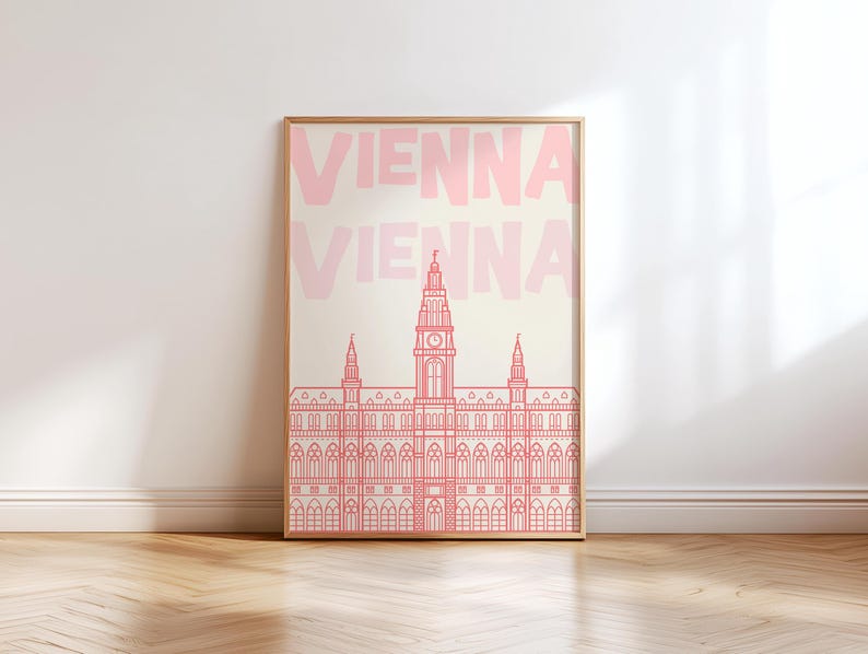 May include: A framed art print featuring a pink line drawing of a building with a clock tower, set against a cream background. The word "VIENNA" is repeated in pink at the top. The artwork is displayed on a wooden floor.