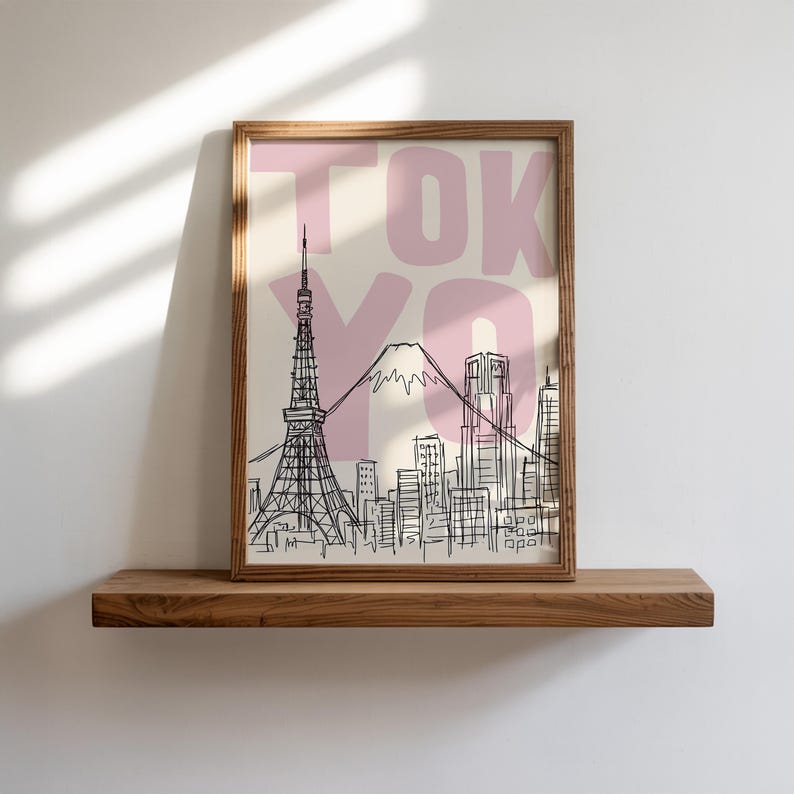 May include: A framed art print featuring a black and white sketch of the Tokyo skyline, including the Tokyo Tower and Mount Fuji. The word "TOKYO" is printed in pink over the image. The print is displayed on a wooden shelf.