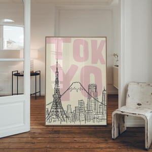 May include: A framed art print featuring a black and white line drawing of the Tokyo skyline, including the Tokyo Tower and Mount Fuji. The word "TOKYO" is printed in large pink letters across the top. The background is a light beige color.