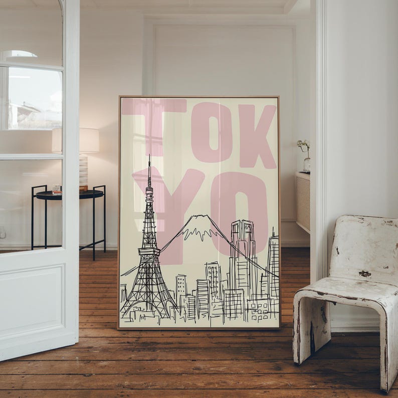 May include: A framed art print featuring a black and white line drawing of the Tokyo skyline, including the Tokyo Tower and Mount Fuji. The word "TOKYO" is printed in large pink letters across the top. The background is a light beige color.