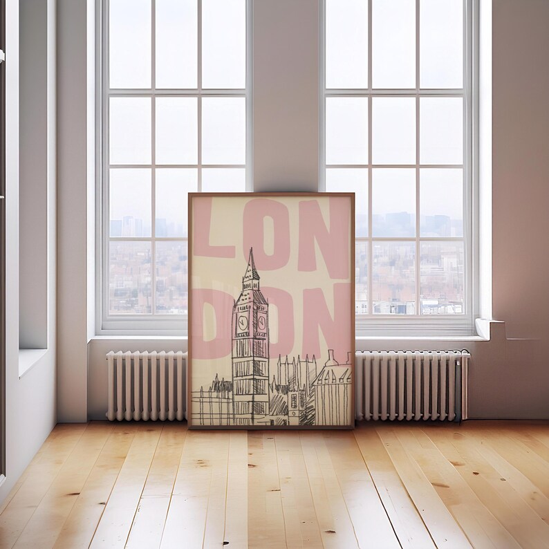 May include: A framed art print featuring a sketch of the Elizabeth Tower, commonly known as Big Ben, in London. The word "LONDON" is printed in large pink letters over the image. The artwork is displayed on a wooden floor in front of a window.