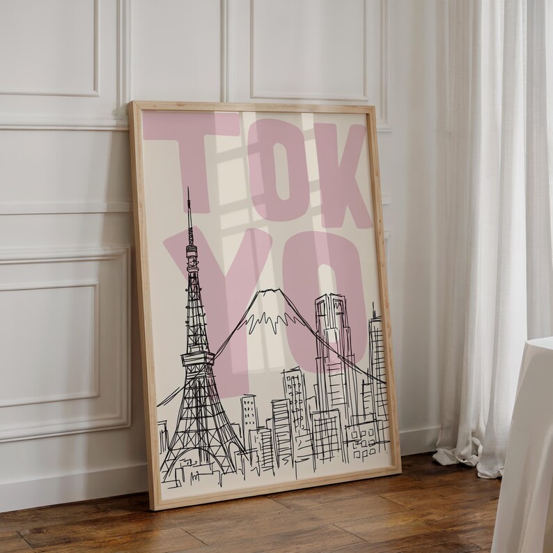 May include: A framed art print featuring a black and white line drawing of Tokyo's skyline, including the Tokyo Tower and Mount Fuji. The word "TOKYO" is printed in large, pink letters over the image. The print is in a light wood frame.
