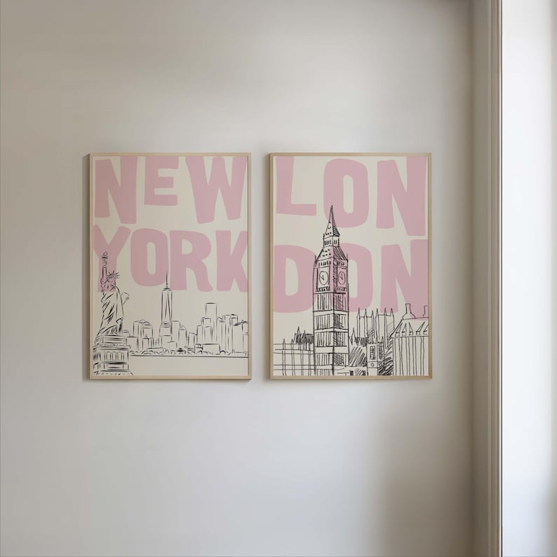 May include: Two framed art prints featuring cityscapes. One print displays the New York City skyline with the Statue of Liberty, and the other showcases London's Big Ben. The words "NEW YORK" and "LONDON" are in pink block letters.