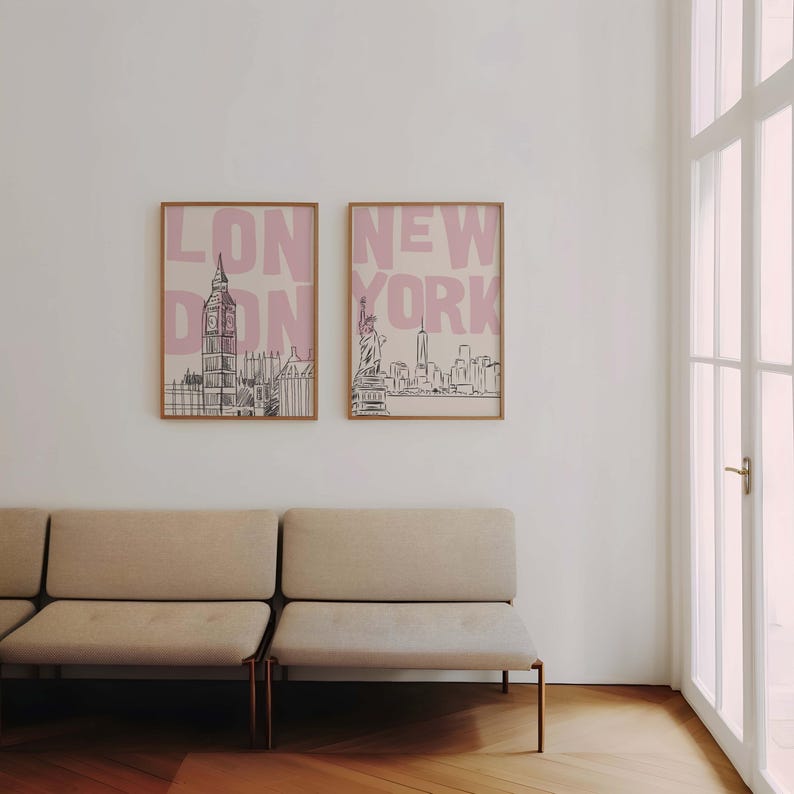 May include: Two framed art prints featuring cityscapes. One print displays the London skyline with the text "LONDON" in pink, and the other showcases the New York skyline with the text "NEW YORK" in pink. The frames are a light brown color.
