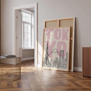 May include: A framed art print featuring a black and white illustration of the Tokyo skyline, including the Tokyo Tower and Mount Fuji, with the word "TOKYO" in pink. The print is leaning against a larger, unframed canvas.