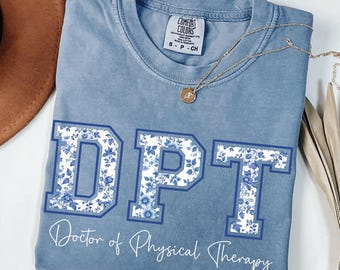 May include: A light blue t-shirt with a white background and blue floral pattern. The letters DPT are printed in a blue outline with the floral pattern inside. The text "Doctor of Physical Therapy" is printed below the letters.