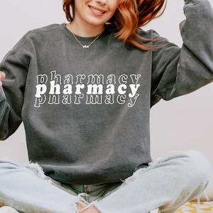 May include: A dark gray sweatshirt with the word "pharmacy" printed three times in white, with each word slightly offset from the one above it.