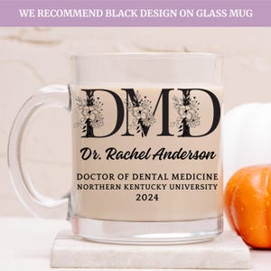 Puede incluir: Una taza de vidrio transparente con un diseño negro que dice "DMD" con acentos florales. El texto debajo dice "Dr. Rachel Anderson, Doctor en Medicina Dental, Universidad del Norte de Kentucky, 2024".