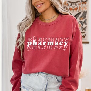 May include: A red long-sleeved sweatshirt with the word "pharmacy" printed three times in white, stacked on top of each other in a retro font.