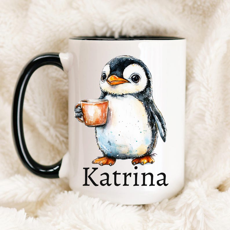 May include: White ceramic mug with a black handle and rim, featuring a watercolor illustration of a penguin holding a small orange cup. The penguin has black and white feathers and the name "Katrina" is printed below.