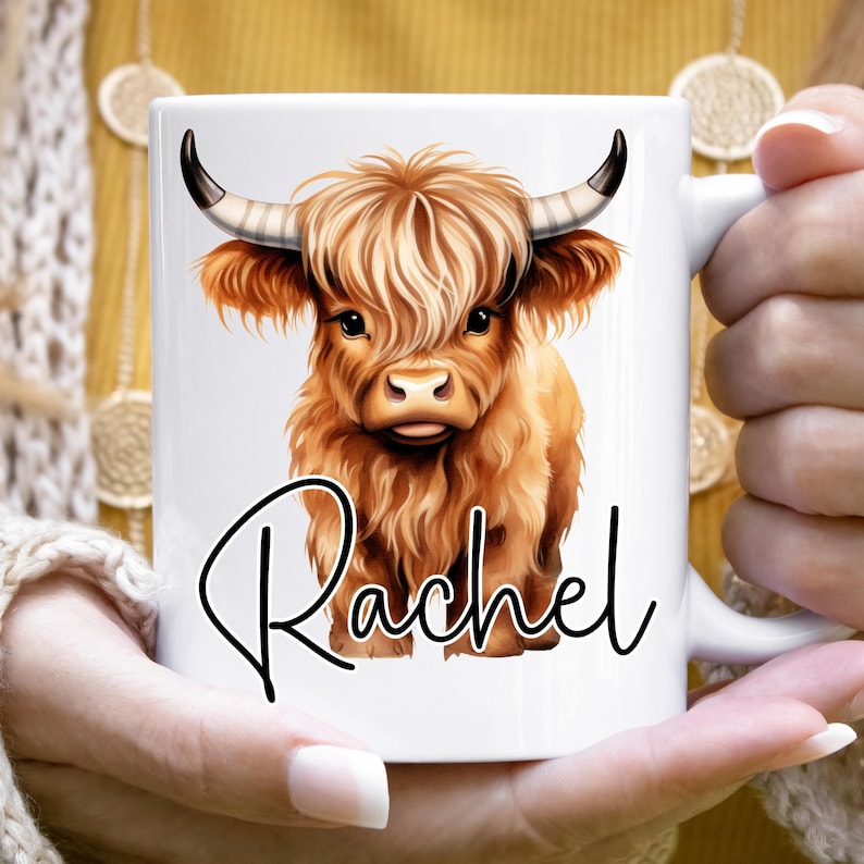 Może przedstawiać: Biały kubek ceramiczny z ilustracją brązowej i białej krowy szkockiej g&oacute;rskiej i imieniem "Rachel" napisanym czarnym, ozdobnym pismem.