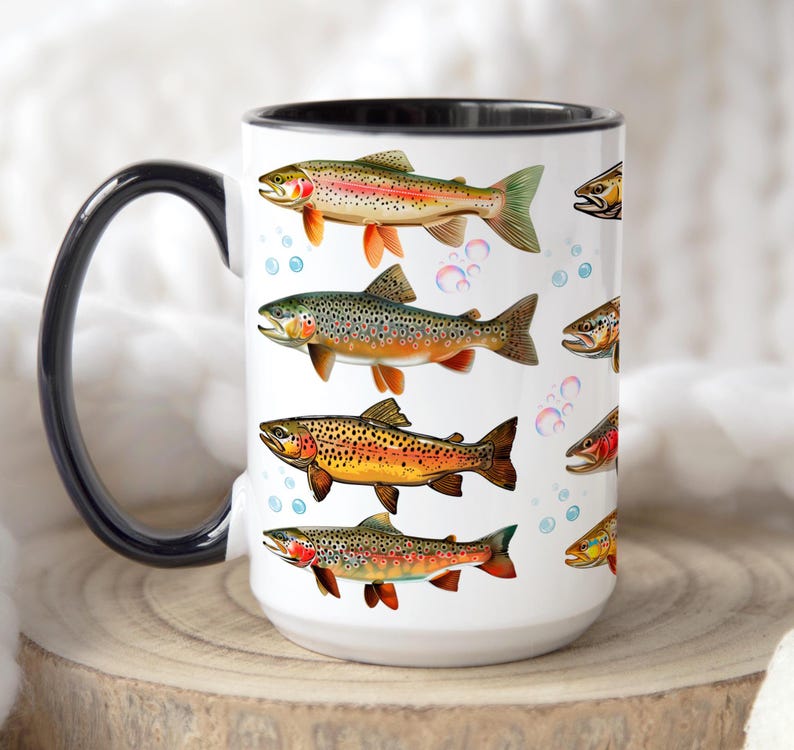May include: White ceramic mug featuring colorful illustrations of various trout species. The mug has a black handle and rim, with bubbles scattered around the fish. The design includes rainbow trout, brown trout, and other fish, making it a great gift for fishing enthusiasts.