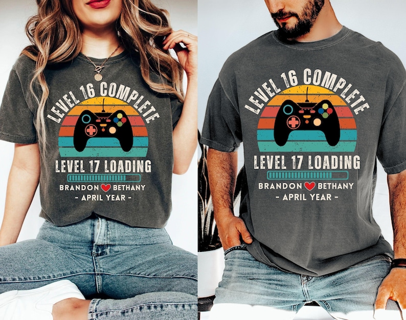 May include: Two gray t-shirts with a retro video game controller graphic and the text "Level 16 Complete" and "Level 17 Loading". The shirts also include the text "Brandon Bethany - April Year - "