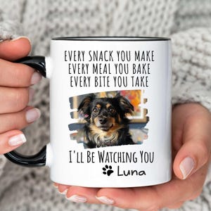 May include: White ceramic mug with a black rim and handle. The mug features a photo of a small black and brown dog with the text "EVERY SNACK YOU MAKE EVERY MEAL YOU BAKE EVERY BITE YOU TAKE I'LL BE WATCHING YOU Luna".