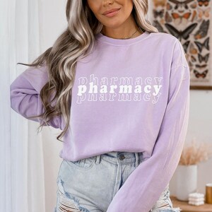 May include: A lavender long-sleeve shirt with the text "pharmacy" printed in white in a retro font.