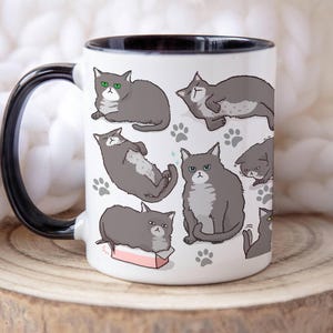 May include: White ceramic mug with a black rim and handle. The mug features a repeating pattern of gray cats in various poses, including sleeping, sitting, and playing. The cats have green eyes and white markings.