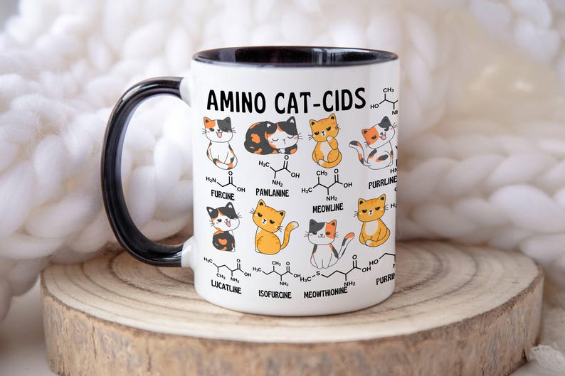Może przedstawiać: Biały kubek ceramiczny z czarnym uchwytem i czarnym rantem. Kubek przedstawia grafikę z kresk&oacute;wkowymi kotami z wzorami chemicznymi i tekstem "AMINO CAT-CIDS".