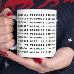 May include: White ceramic mug with a black design of binary code. The code is repeated in rows and columns on the mug.