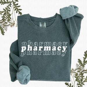 May include: A teal blue sweatshirt with the word "pharmacy" written in white, stacked three times with each word slightly offset from the one above it.