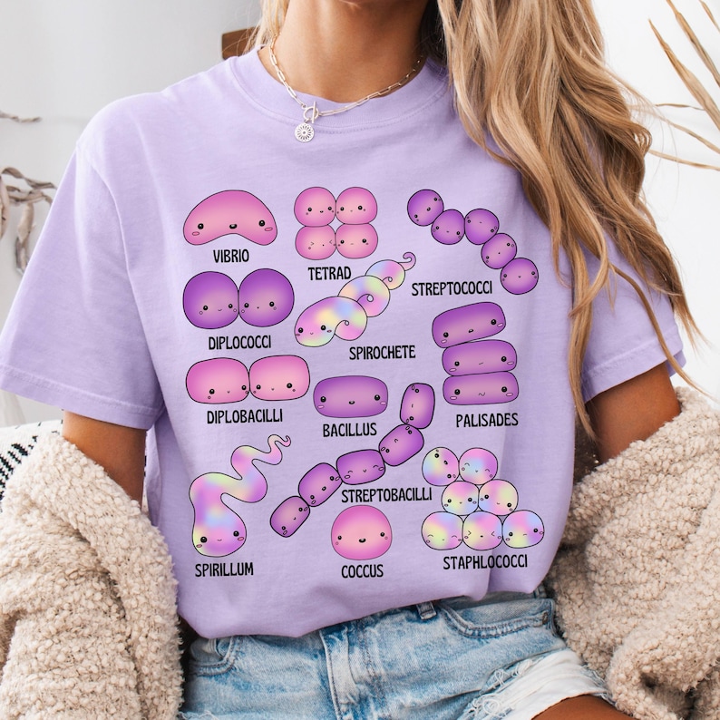 May include: A lilac t-shirt displaying cartoon bacteria illustrations, such as Vibrio, Tetrad, and Spirochete. Each bacterium is uniquely shaped and labelled with its name in black text. The t-shirt is a casual style.