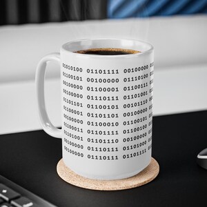 Może przedstawiać: Biały ceramiczny kubek z powtarzającym się wzorem czarnych cyfr kodu binarnego nadrukowanych na zewnętrznej powierzchni. Kubek posiada zakrzywione ucho po lewej stronie i jest wypełniony ciemnym płynem, z kt&oacute;rego unosi się para wodna.