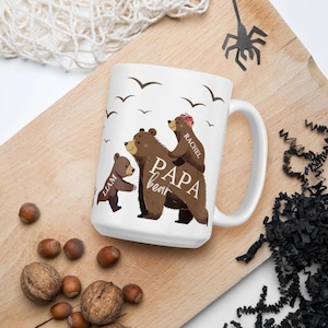 Może przedstawiać: Biały kubek ceramiczny z wzorem rodziny brązowych niedźwiedzi. Niedźwiedź tata jest oznaczony jako "Papa Bear", a niedźwiedź mama jako "Rachel". Mały niedźwiedź jest oznaczony jako "Liam".