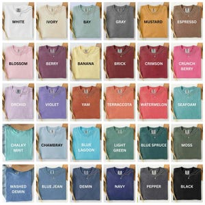 Op de afbeelding: Een verzameling gevouwen t-shirts in verschillende kleuren, waaronder wit, ivoor, baai, grijs, mosterd, espresso, bloesem, bes, banaan, baksteen, karmozijn, crunch berry, orchidee, violet, yam, terracotta, watermeloen, schuim, krijtachtige munt, chambray, blauwe lagune, lichtgroen, blauwe spar, mos, gewassen demin, blauwe spijkerbroek, demin, marine, peper en zwart.