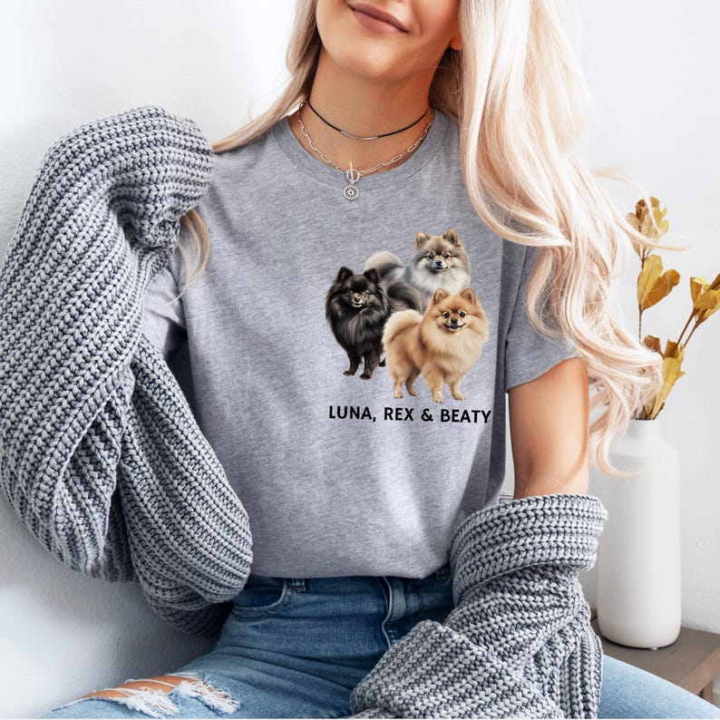 May include: A gray t-shirt with a graphic of three Pomeranian dogs. The dogs are brown, black, and gray. The text "LUNA, REX & BEATY" is printed below the dogs.