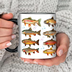 May include: White ceramic mug with a black handle and rim, featuring colorful illustrations of various fish species. The fish are depicted in detail with vibrant colors and scales, set against a white background with blue bubbles.