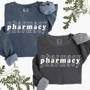 May include: Two sweatshirts with the word "pharmacy" printed on them in a retro style. The sweatshirts are in different shades of blue and gray.