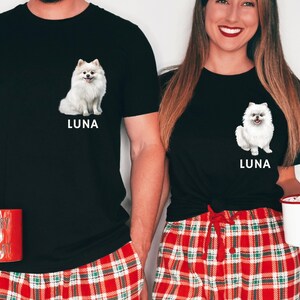 May include: Two people wearing black t-shirts with a white dog illustration and the name "Luna" printed on them. They are wearing red and green plaid pajama pants. The person on the left is holding a red mug with the text "Merry & Bright".