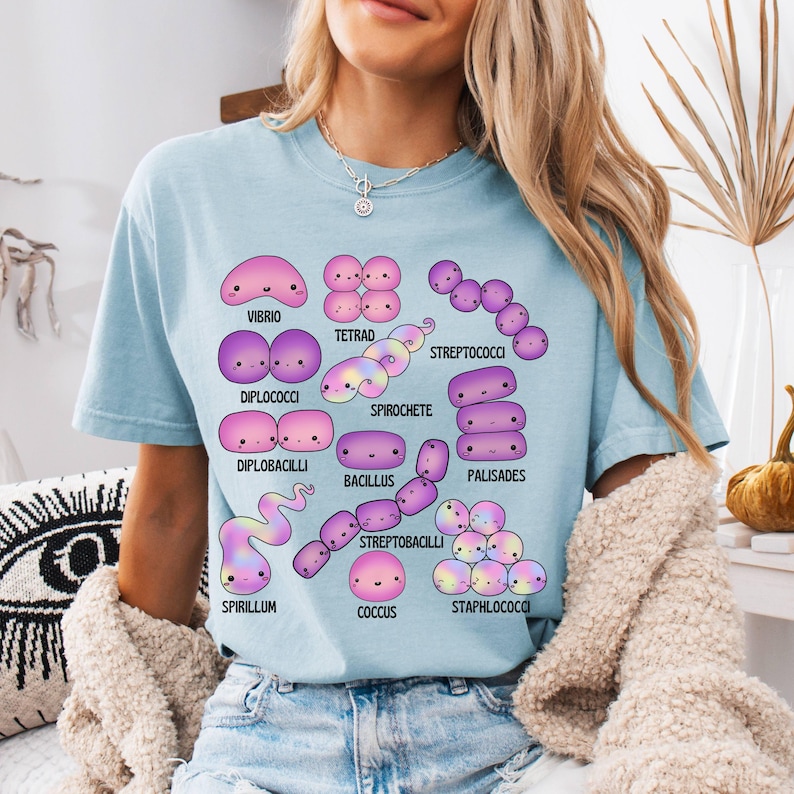 May include: Pale blue t-shirt displaying a vibrant illustration of different bacteria, such as Vibrio, Tetrad, and Spirochete. Each bacterium is designed in a cute, cartoon style and labelled with its name in white text.