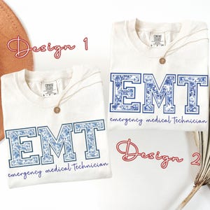 Puede incluir: Dos camisetas blanquecinas con las letras "EMT" en estampado floral azul. El texto "emergency medical technician" est&aacute; debajo de las letras. Una camiseta tiene un collar dorado. Las palabras "Design 1" y "Design 2" est&aacute;n escritas en cursiva.