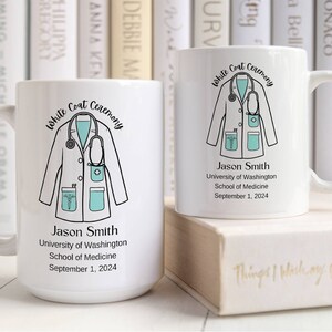 May include: White ceramic mug with a black and white illustration of a doctor's coat with a stethoscope. The mug has the text "White Coat Ceremony" and "Jason Smith" along with the University of Washington School of Medicine and the date September 1, 2024.