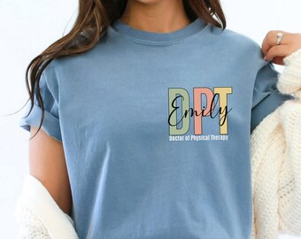 May include: A light blue t-shirt with the text "DPT Emily Doctor of Physical Therapy" in a colorful design. The letters "DPT" are in green, pink, and yellow. The name "Emily" is in a cursive font.